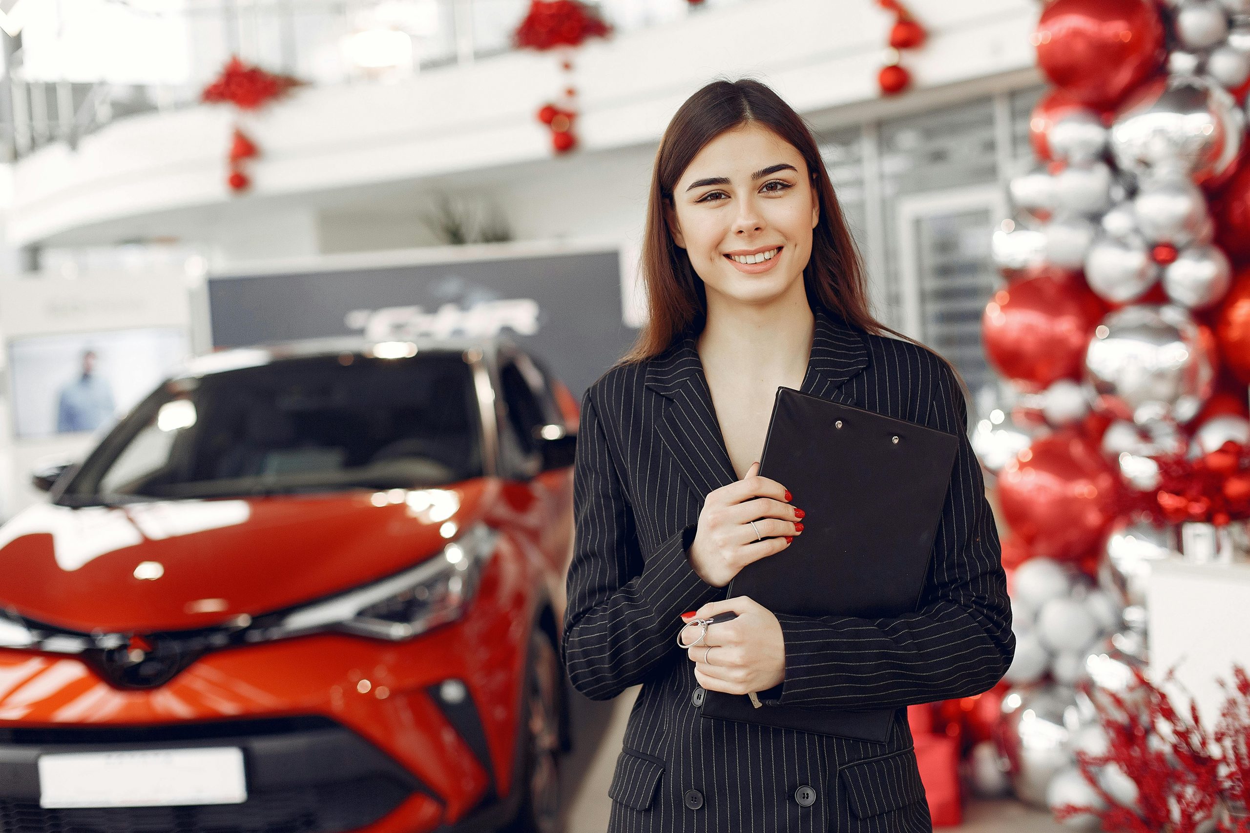 Caucasian woman in business attire smiling at camera in a car showroom decorated for holidays.